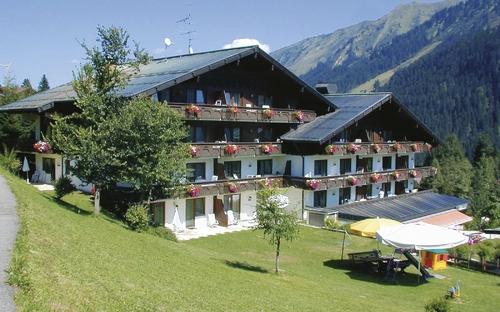 Hotelgebäude in alpiner Landschaft mit Balkonen und Sommerblumen.