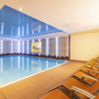 Hallenbad mit blauen Fliesen und orangefarbenen Liegestühlen im Hotel Alpenrose.