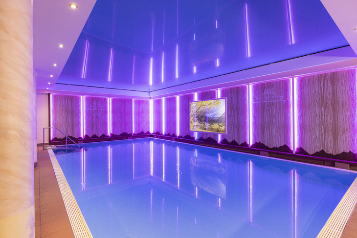 Innenpool des Hotels Alpenrose mit violetter Beleuchtung und Bergwandbild.
