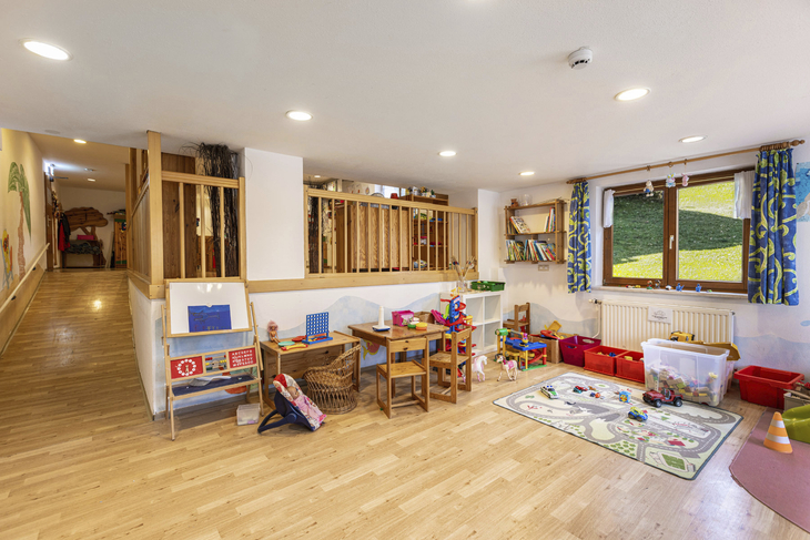 Spielzimmer für Kinder mit Tischen, Spielzeug und bunten Vorhängen.