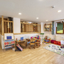 Spielzimmer für Kinder mit Tischen, Spielzeug und bunten Vorhängen.
