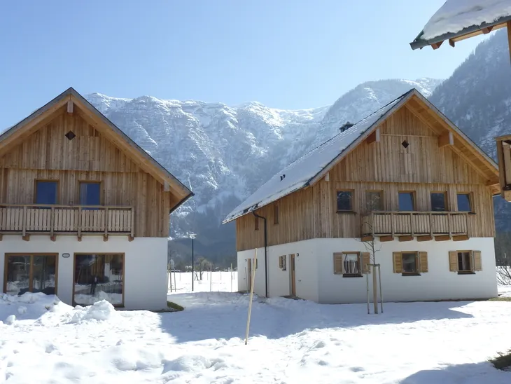 Zwei Chalets im Schnee vor Bergkulisse bei klarem Himmel.