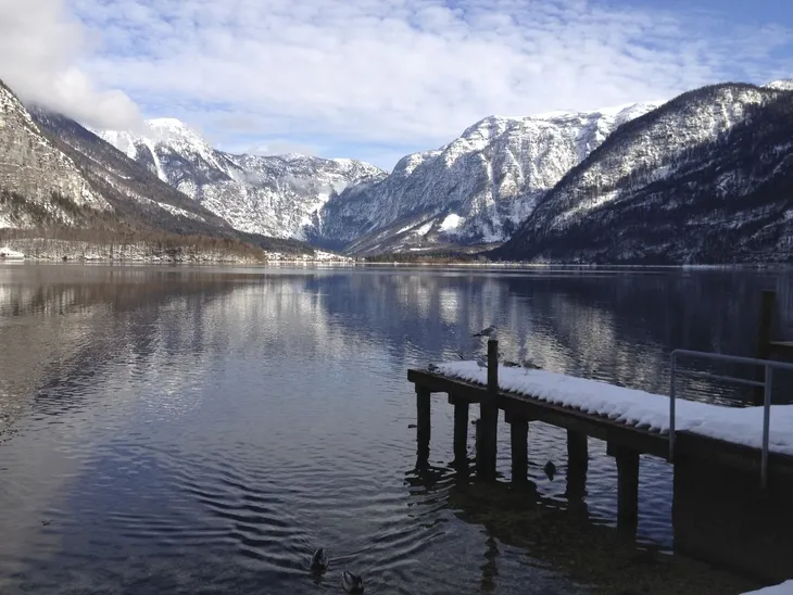 Landschaft mit See, schneebedeckten Bergen und einem Steg im Vordergrund.