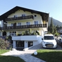 Gelbes Haus mit Holzdetails, zwei Autos davor, in bergiger Umgebung.