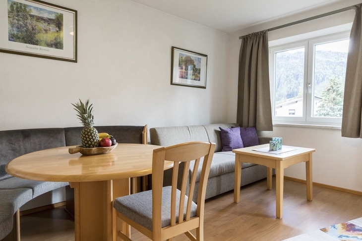 Wohnzimmer mit Holzmöbeln, Esstisch, Sofa, Bildern und Fenster mit Bergblick.