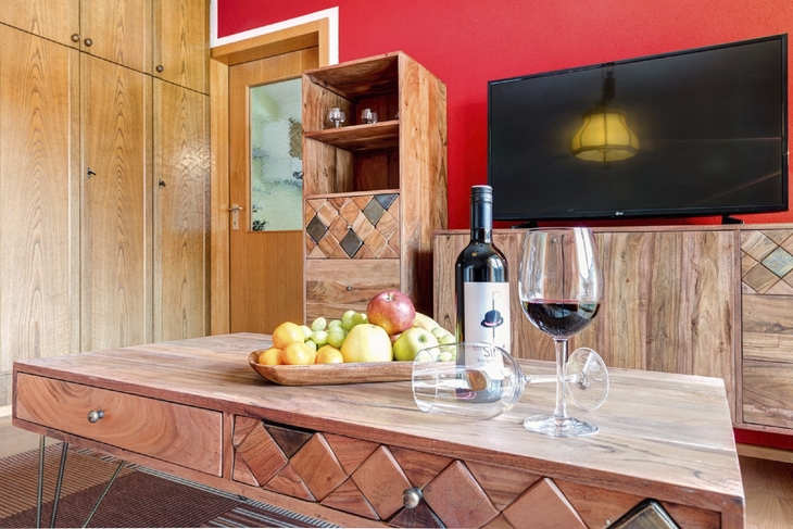 Wohnzimmer mit Holzmöbeln, Flachbildfernseher, Obstschale und Weinflasche auf dem Tisch.