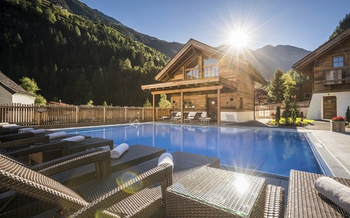 Außenansicht eines Wellness-Hüttendorfs mit Pool und Sonnenuntergang in den Bergen.