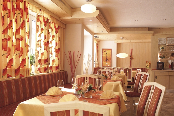 Speisesaal mit gedeckten Tischen und bunten Vorhängen in warmen Farben.