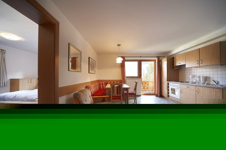 Wohnzimmer mit Küchenzeile, Esstisch und Zugang zu einem Balkon.