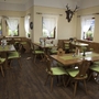 Restaurantbereich mit Holzstühlen, grünen Kissen und Vorhängen, Tageslicht durch Fenster.