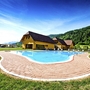 Pool vor gelben Gebäuden auf einem Campingplatz in Hügel- und Waldlandschaft.