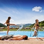 Drei Personen entspannen am Pool vor einer hügeligen Landschaft.