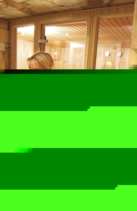Person im Bademantel vor Sauna mit sitzendem Mann innen.
