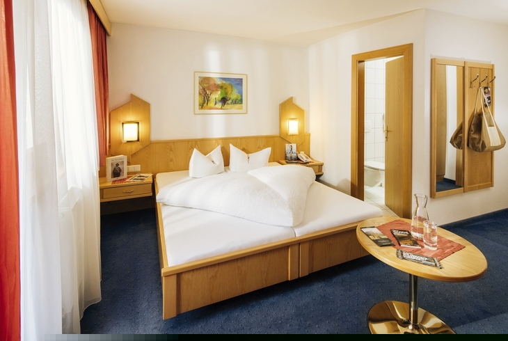 Hell eingerichtetes Hotelzimmer mit Doppelbett, Nachtlampen und Tisch.