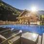 Außenansicht eines Wellness-Hüttendorfs mit Pool und Sonnenuntergang in den Bergen.