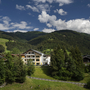 Hotel in Wagrain umgeben von grünen Bergen und blauem Himmel.
