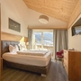Helles Hotelzimmer mit Doppelbett, Holzmöbeln und großer Fensterfront mit Bergblick.