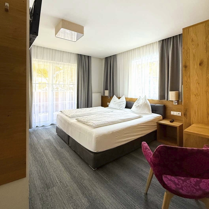 Modern eingerichtetes Hotelzimmer mit Doppelbett und lila Sessel.