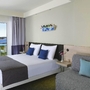 Hotelzimmer mit Doppelbett, Sofa und Blick aufs Meer durch Fenster.