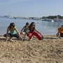 Menschen dehnen sich am Strand mit Meer und Booten im Hintergrund.