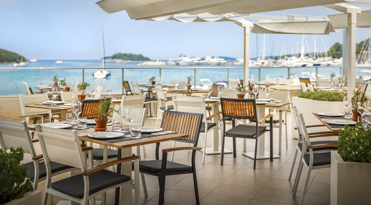 Außenterrasse eines Restaurants mit Blick auf das Meer und Segelboote.