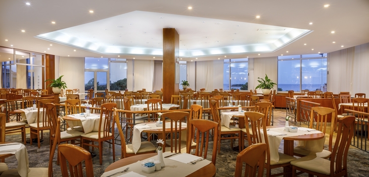 Geräumiges Hotelrestaurant mit Holzstühlen und großen Fenstern, Blick auf das Meer.