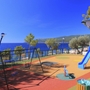 Spielplatz mit Klettergerüst und Rutsche, Meer im Hintergrund, sonniger Tag.