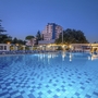 Außenansicht eines Hotels bei Abenddämmerung mit beleuchtetem Pool im Vordergrund.
