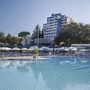 Hotelpool mit Liegestühlen, Bäumen im Hintergrund und einem Gebäudekomplex.