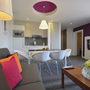 Modernes Wohnzimmer mit Küchenzeile, bunten Kissen und Blumenarrangement.