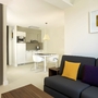 Modernes Studio-Apartment mit Küche und Wohnbereich, dunkles Sofa und bunte Kissen.