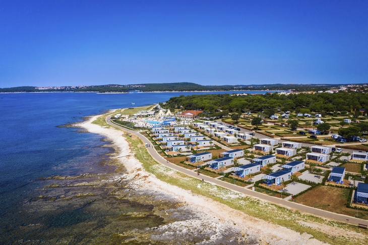 Luftaufnahme von Mobilheimen am Meer, umgeben von Wald und Küste.