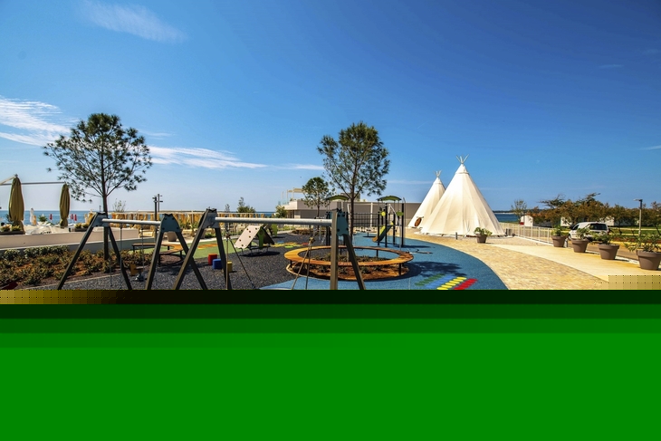 Spielplatz im Freien mit Schaukeln und Tipis unter blauem Himmel.