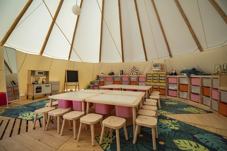Innenansicht eines bunt gestalteten Kinderspielzimmers mit Tischen und Sitzhockern.