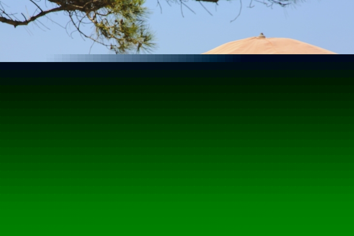 Strand mit orangefarbenem Boot, Sonnenschirm und Liegestühlen am Meer.
