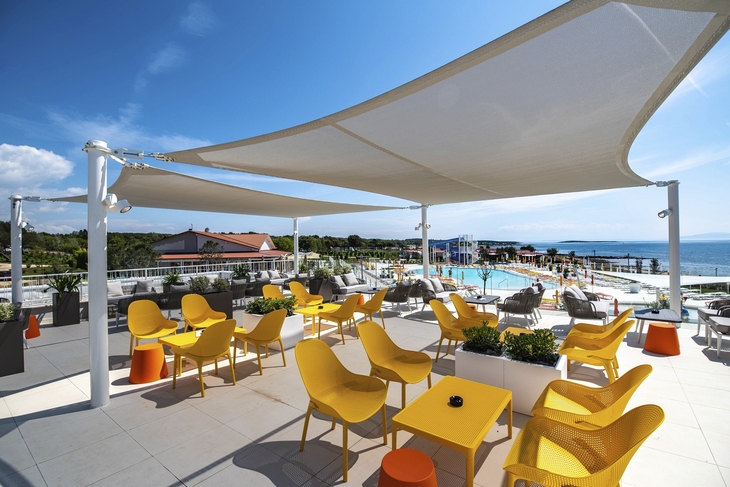 Terrasse mit gelben Stühlen, Sonnensegel und Blick auf Pool und Meer.