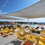 Terrasse mit gelben Stühlen, Sonnensegel und Blick auf Pool und Meer.