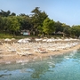 Strand mit Sonnenliegen und Sonnenschirmen am klaren Wasser, umgeben von Bäumen.