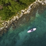 Person auf Paddleboard auf klarem Wasser neben felsiger Küste und bewaldetem Ufer.