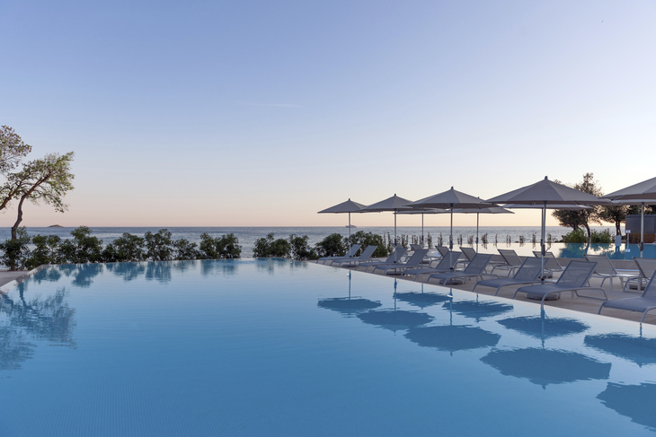 Infinity-Pool mit Liegestühlen und Sonnenschirmen, Meerblick im Hintergrund.