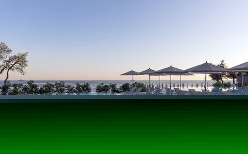 Infinity-Pool mit Liegestühlen und Sonnenschirmen, Meerblick im Hintergrund.