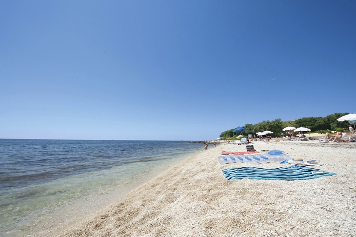 Strand mit Liegestühlen und Sonnenschirmen am Meer unter klarem Himmel.