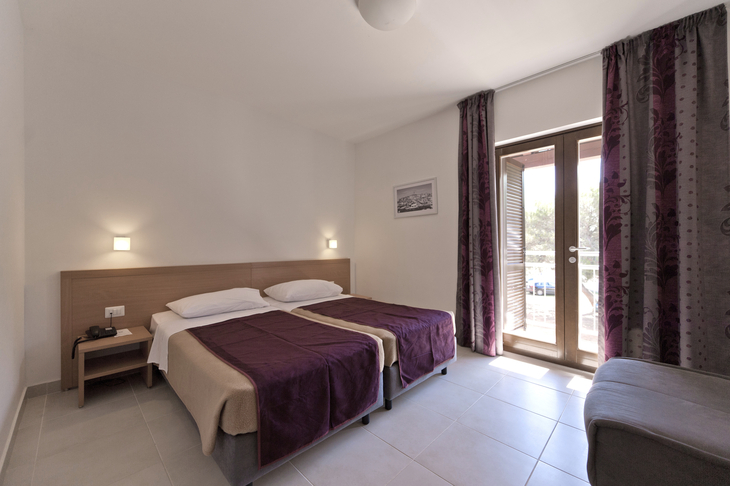Helles Hotelzimmer mit zwei Einzelbetten, Nachttisch und Balkonzugang.