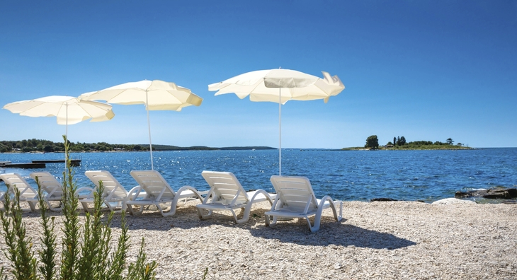 Strand mit Liegestühlen und weißen Sonnenschirmen am Meer.