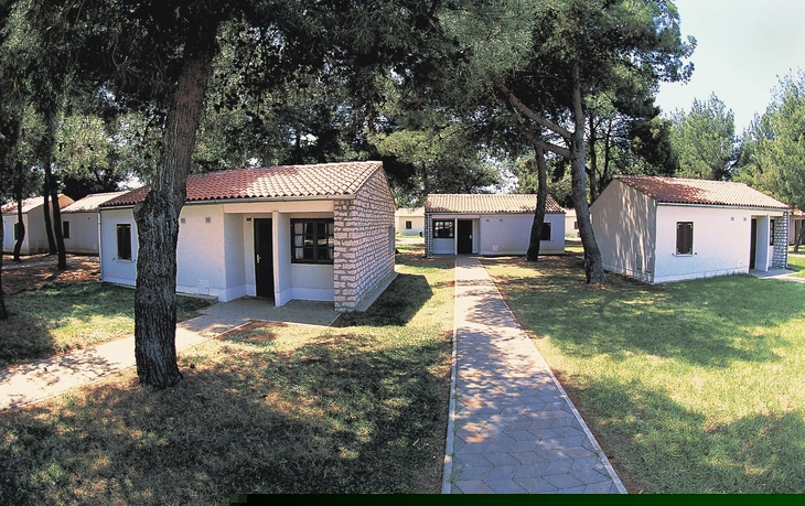 Bungalows im Grünen mit gepflasterten Wegen und umgebenden Bäumen.