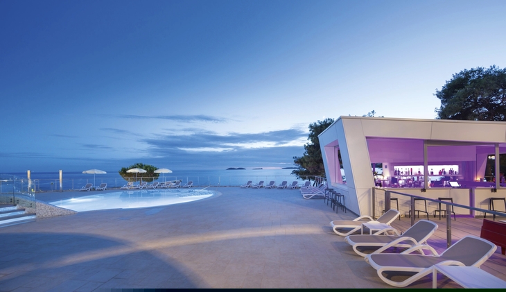 Poolbar bei Sonnenuntergang mit Blick aufs Meer und Liegestühlen