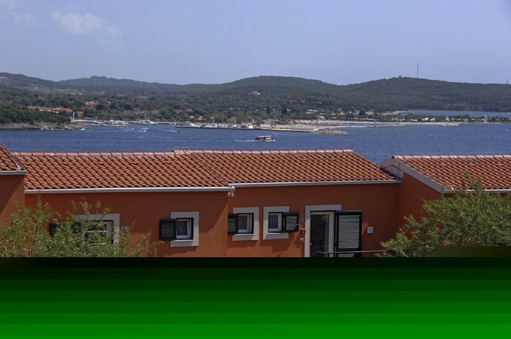Gebäude mit orangen Dächern vor Küstenlandschaft und blauem Wasser.