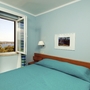 Schlafzimmer mit offenem Fenster, Blick auf Landschaft, blau-grüne Vorhänge.
