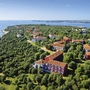 Luftaufnahme eines Küstenresorts mit roten Dächern, umgeben von Bäumen und Meer.