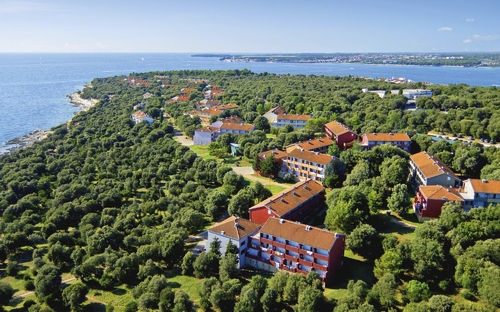 Luftaufnahme eines Küstenresorts mit roten Dächern, umgeben von Bäumen und Meer.